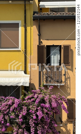 Colorful Italian Facade with Flowering Bush and Wooden Shutters in Bright Sunlight in Sirmione 121652144