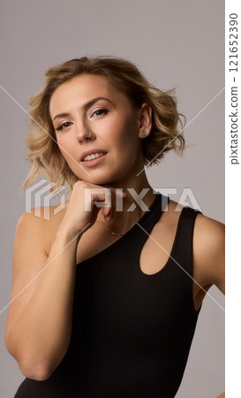 Confident Woman with Short Wavy Hair Wearing a Stylish Black Outfit in a Studio Setting 121652390