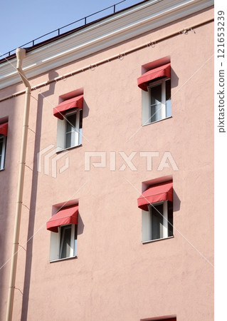 classic-style historic pink house with red awnings on windows. sunny day. stylish architecture 121653239