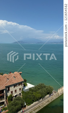 Serene Lakeside View with a Coastal Italian House and Vibrant Blue Waters of Lake Garda Serene Lakeside View with a Coastal Italian House and Vibrant Blue Waters of Lake Garda 121654582