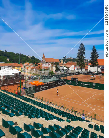 Tennis courts with stands. In the city of Brasov in Romania, tennis courts are seen against the backdrop of houses and a church in the background. 121654990