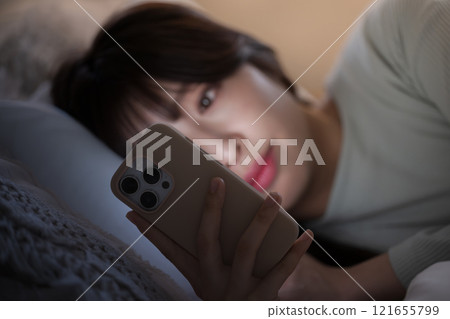 Close-up of a woman looking at her smartphone in the middle of the night and feeling sleep deprived 121655799