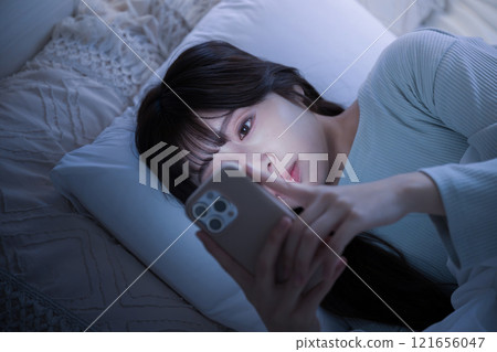 Close-up of a woman looking at her smartphone in the middle of the night and not getting enough sleep. Blue color 121656047