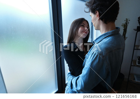 Young couple sharing a tender moment indoors by a window during daylight 121656168