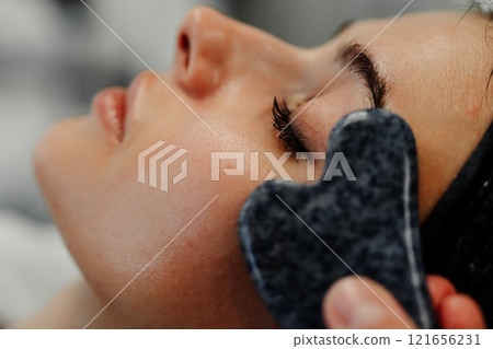 Relaxing facial treatment using gua sha tool at spa during afternoon session Relaxing facial treatment using gua sha tool at spa during afternoon session 121656231