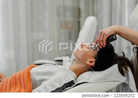 Woman receiving relaxing facial treatment at spa during afternoon in modern wellness studio 121656252