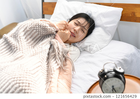 年輕的亞洲女子在床上看起來很痛苦 年輕的亞洲女子在床上看起來很痛苦 121656429