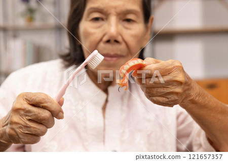 Elderly Woman Cleaning Dentures with a Toothbrush. Elderly Woman Cleaning Dentures with a Toothbrush. 121657357