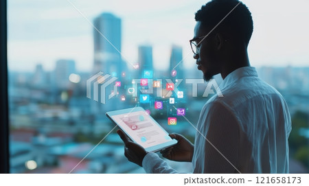 Businessman is holding a tablet with holographic social media icons emerging, showcasing the integration of technology and social networks in a modern office setting with a stunning city view 121658173