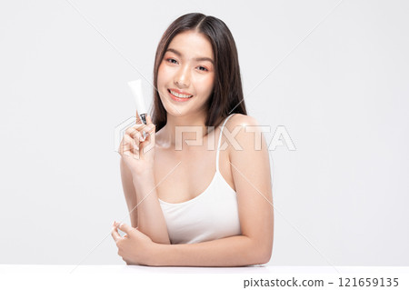 Beautiful Asian woman with a radiant smile holding a blank tube, ready for your cosmetic or skincare branding. Confidence and elegance personified isolated on white background. Self Care Concept 121659135