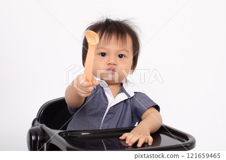 Cute Asian Baby Holding Spoon While Sitting in High Chair 121659465