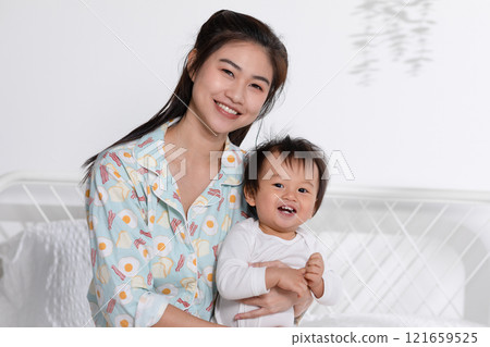 Cute Asian mom hugging her baby boy on bed smile and happiness together. Little baby toddler sit on bed and relax with mother speding time to learning and growth. Good momen of family time. Mother day 121659525