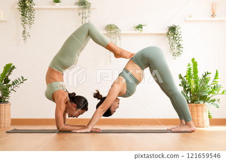 Couple and paired Asian young woman on yoga mat doing breathing exercise yoga together.Yoga meditation of two healthy female balancing body and relax at cozy home. Self care concept 121659546
