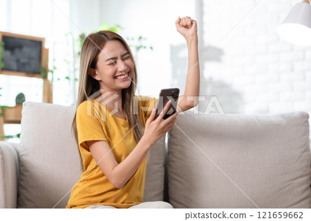 Exuberant young woman in a yellow t-shirt jubilantly celebrating good news on her mobile phone 121659662