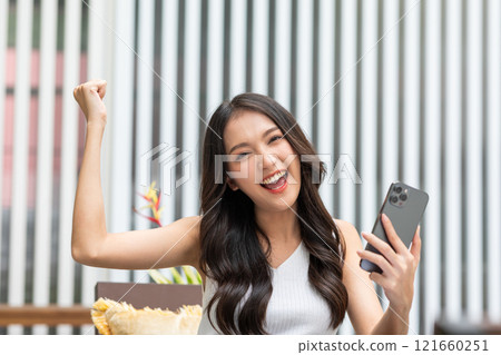 Millennial asian young woman looking mobile phone laughing with good news or discount voucher for shopping online at home.Happy and cheerful woman looking on cellphone app read message feel excited 121660251
