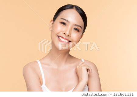 A cheerful woman with smooth skin and a bright smile, showcasing natural beauty against a warm orange background. 121661131