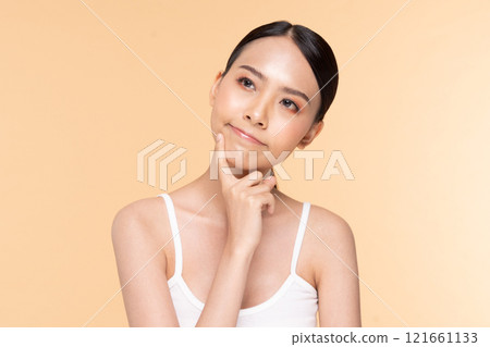 A thoughtful woman poses with a curious expression, contemplating ideas against a warm, neutral backdrop. 121661133