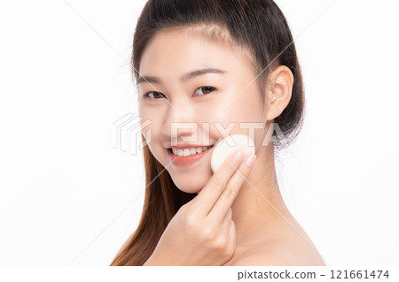 Smiling Asian woman applying foundation with a cosmetic sponge on a white background Smiling Asian woman applying foundation with a cosmetic sponge on a white background 121661474