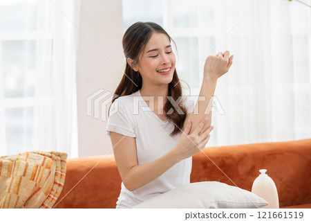 Woman Applying Lotion to Arm in Comfortable Home Setting 121661519
