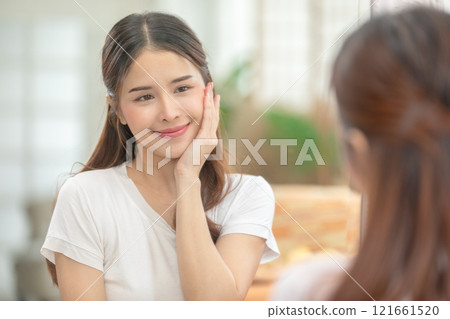 Asian Woman Admiring Smooth Skin in Mirror During Skincare Routine 121661520
