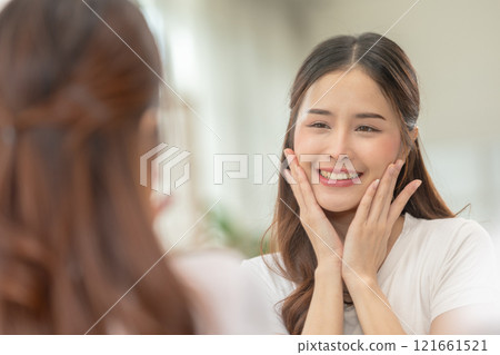 Asian Woman Admiring Smooth Skin in Mirror During Skincare Routine 121661521