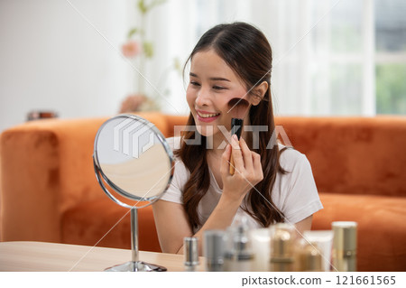 Happy Asian young woman smile and looking in mirror doing skin care applying make up brush on her cheek and beauty treatment at home,Wellness woman self care with beauty product at home Happy Asian young woman smile and looking in mirror doing skin care applying make up brush on her cheek and beauty treatment at home,Wellness woman self care with beauty product at home 121661565