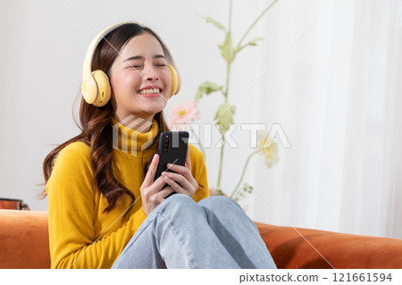 Exuberant young woman in yellow enjoying music with closed eyes, holding a smartphone and wearing headphones 121661594