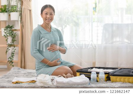 Pregnant woman organizing baby essentials and packing a hospital bag, preparing for the upcoming birth, and smiling with excitement. Pregnant woman organizing baby essentials and packing a hospital bag, preparing for the upcoming birth, and smiling with excitement. 121662147