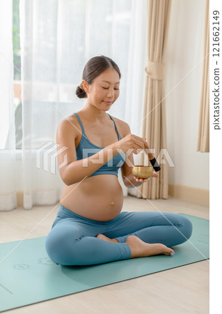 Pregnant woman practices meditation with a singing bowl, promoting relaxation and mindfulness during pregnancy. Calm, serene indoor setting. 121662149