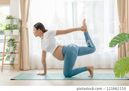 Pregnant woman practicing prenatal yoga at home, stretching on a mat in a bright living room, demonstrating balance and flexibility. 121662150
