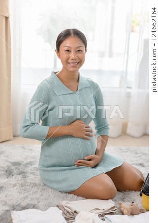 Pregnant woman sitting on the floor at home in a serene and bright room, embracing her belly with a joyful expression. Pregnant woman sitting on the floor at home in a serene and bright room, embracing her belly with a joyful expression. 121662164