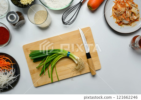 Fresh green onions on a wooden cutting board surrounded by ingredients for preparing traditional Kimchi 121662246