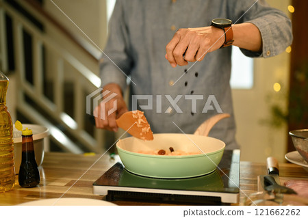 Close up of man adding ingredients to pan while stirring fried rice with a wooden spatula 121662262