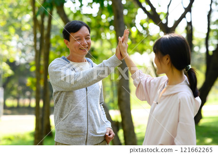 Middle aged man and his daughter giving high five after outdoor workout. Healthy and outdoor activity concept 121662265