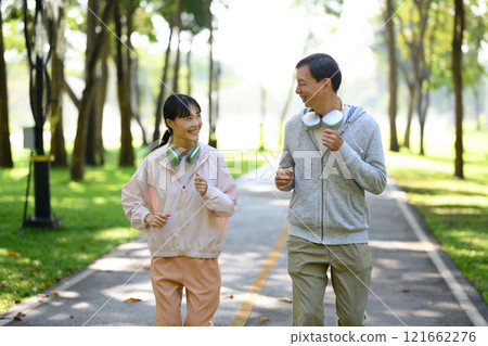 Cheerful older man and daughter jogging together on a paved path in a beautiful park 121662276
