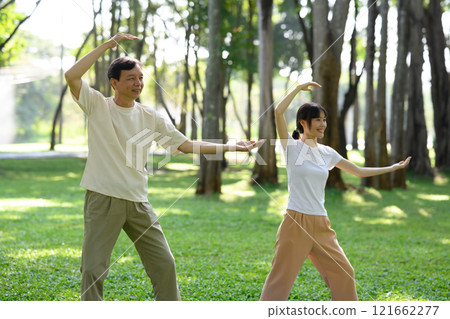 Calm middle aged man and young woman practicing Tai Chi standing in graceful poses on mats in picturesque park Calm middle aged man and young woman practicing Tai Chi standing in graceful poses on mats in picturesque park 121662277