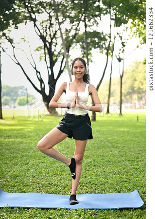 Portrait of African American woman practicing meditation outdoors, standing with praying hands 121662334