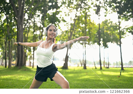 Attractive fit woman wearing headphone practicing yoga on a grassy lawn. Healthy lifestyle concept Attractive fit woman wearing headphone practicing yoga on a grassy lawn. Healthy lifestyle concept 121662366