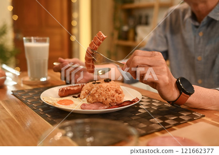 Cropped shot senior man enjoying lunch on wooden table in cozy home kitchen 121662377
