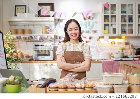 confident woman entrepreneur stands proudly in her kitchen, surrounded by prepared food items neatly packaged for sale. She wearing apron and smiling, exuding sense of accomplishment and professional 121663298