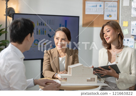 Diverse team of architects and professionals discussing house model in office meeting. The participants are engaged in an in-depth conversation, with architectural drawings displayed in the background Diverse team of architects and professionals discussing house model in office meeting. The participants are engaged in an in-depth conversation, with architectural drawings displayed in the background 121663822