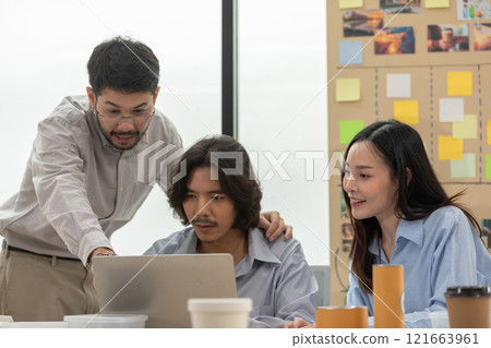 Asian group of colleagues working together on project with one man explaining data on laptop while the others focus attentively. Suggesting creative and organized approach to project management Asian group of colleagues working together on project with one man explaining data on laptop while the others focus attentively. Suggesting creative and organized approach to project management 121663961