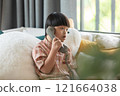 Asian young boy with Down syndrome sits comfortably at home, engaged in a phone conversation. He holds a retro-style telephone, focusing intently on the call 121664038