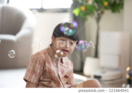 Asian cheerful young boy with Down syndrome enjoys playing with bubbles indoors. His bright smile and playful gestures capture the innocence and joy of childhood Asian cheerful young boy with Down syndrome enjoys playing with bubbles indoors. His bright smile and playful gestures capture the innocence and joy of childhood 121664041