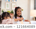 Two young Asian girls with Down syndrome engage in a fun arts and crafts activity, sharing smiles and creativity. They are focused on crafting with colorful materials 121664089