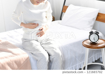 Young Asian woman holding her stomach on the bed Young Asian woman holding her stomach on the bed 121665782