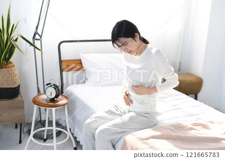 Young Asian woman holding her stomach on the bed 121665783