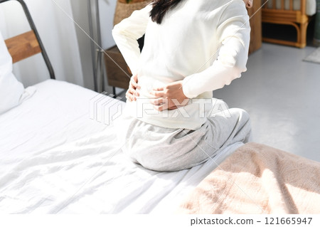 一名年輕女子將腰抱在床上的後視圖 一名年輕女子將腰抱在床上的後視圖 121665947