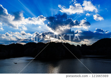 A cold wind-swept evening at Nara Nunome Dam in the New Year: Sunlight shining through the clouds against a blue sky and a light trail on the lake surface① 121665989