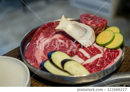 A close-up shot of premium cuts of marbled Hanwoo beef placed on a metal tray, with sliced eggplant and zucchini and eryngii mushroom A close-up shot of premium cuts of marbled Hanwoo beef placed on a metal tray, with sliced eggplant and zucchini and eryngii mushroom 121666217